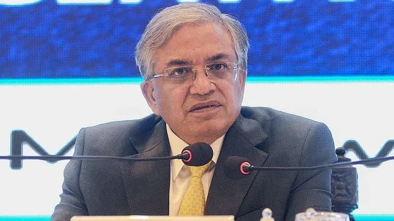 ایک شخص سوٹ اور ٹائی پہنے مائیکروفون کے سامنے بیٹھا ہے۔